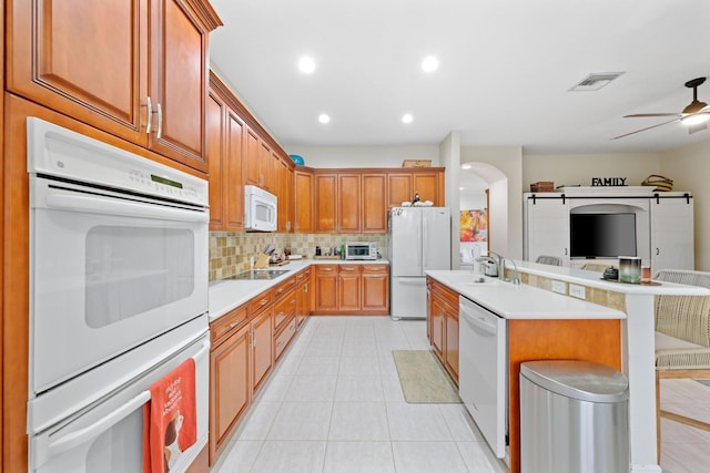 kitchen featuring sink, a breakfast bar area, backsplash, ceiling fan, and white appliances