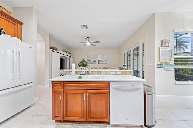 kitchen featuring sink, white appliances, light tile patterned floors, a kitchen island with sink, and a barn door