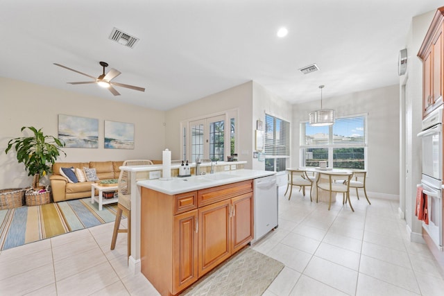 kitchen with hanging light fixtures, light tile patterned floors, an island with sink, white appliances, and ceiling fan with notable chandelier