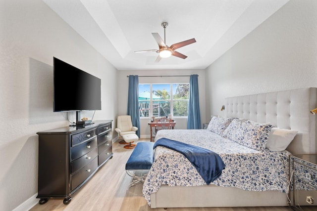 bedroom with light hardwood / wood-style floors, a raised ceiling, and ceiling fan