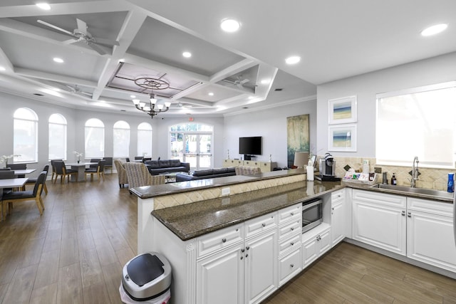 kitchen with coffered ceiling, dark stone countertops, kitchen peninsula, and white cabinets