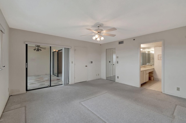 unfurnished bedroom featuring light colored carpet, visible vents, ensuite bathroom, and two closets