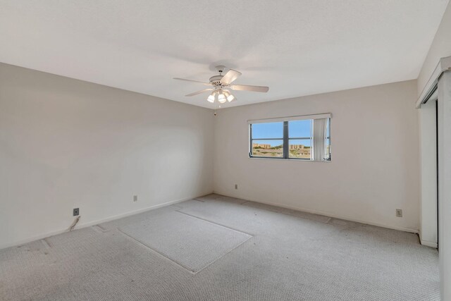 spare room featuring a ceiling fan, light carpet, and baseboards