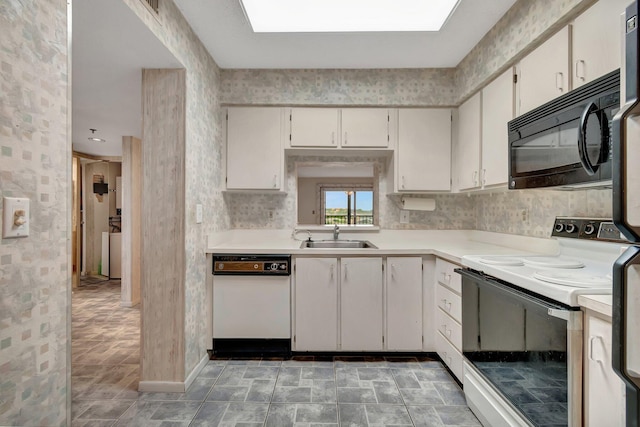 kitchen with white appliances, wallpapered walls, a skylight, light countertops, and a sink