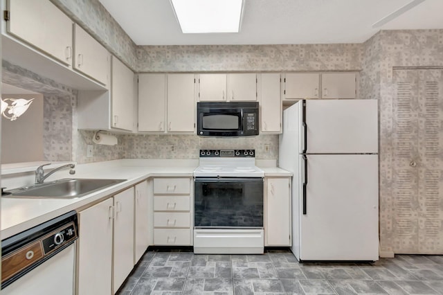 kitchen with light countertops, stone finish flooring, a sink, white appliances, and wallpapered walls