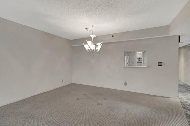 carpeted spare room with a notable chandelier and a textured ceiling