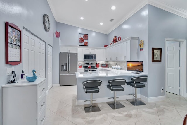 kitchen with appliances with stainless steel finishes, a breakfast bar area, white cabinets, backsplash, and kitchen peninsula