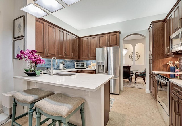 kitchen featuring appliances with stainless steel finishes, light countertops, a peninsula, and a breakfast bar area