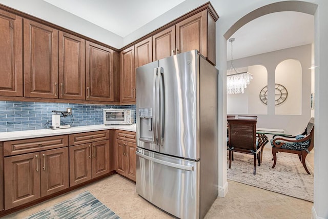 kitchen featuring tasteful backsplash, stainless steel fridge, a toaster, brown cabinets, and light countertops