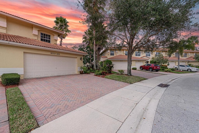 view of front of house with a garage, a residential view, a tiled roof, decorative driveway, and stucco siding