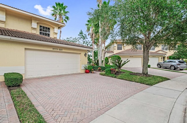 view of front of house featuring a garage, decorative driveway, a tile roof, and stucco siding