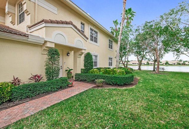 view of front of property with a water view, a tile roof, a front lawn, and stucco siding