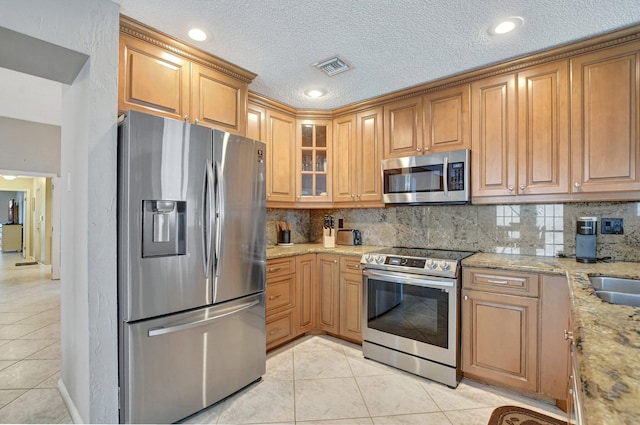 kitchen with light tile patterned flooring, stainless steel appliances, light stone counters, and backsplash