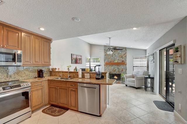 kitchen with lofted ceiling, a stone fireplace, sink, kitchen peninsula, and stainless steel appliances