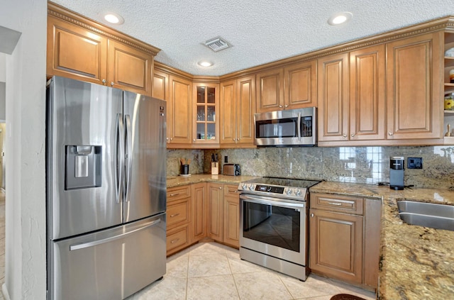 kitchen with light tile patterned flooring, appliances with stainless steel finishes, sink, decorative backsplash, and light stone counters