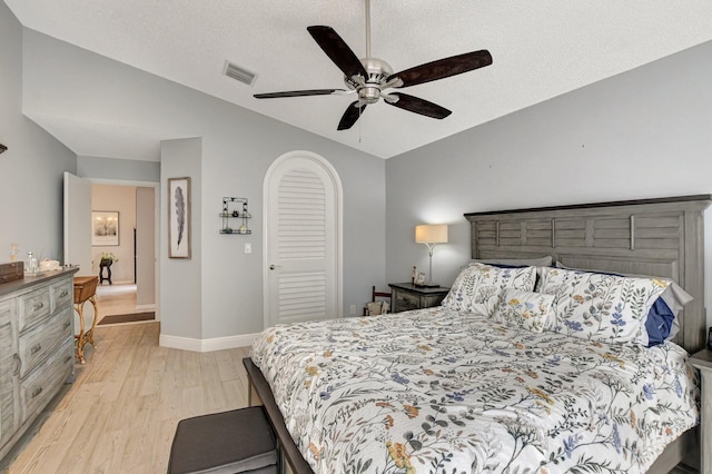 bedroom with vaulted ceiling, a textured ceiling, light wood-type flooring, a closet, and ceiling fan