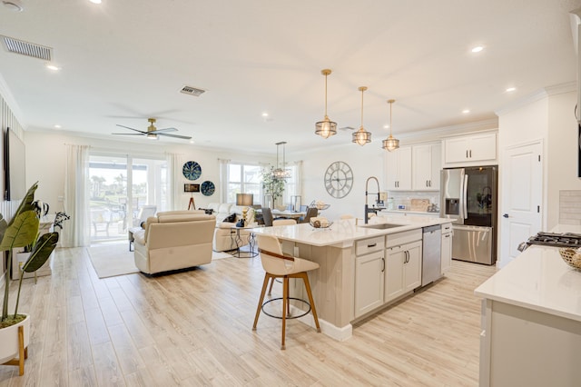 kitchen featuring appliances with stainless steel finishes, decorative light fixtures, white cabinetry, an island with sink, and sink