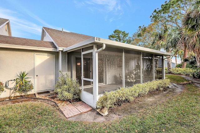 view of property exterior featuring a shingled roof, a sunroom, a yard, and stucco siding