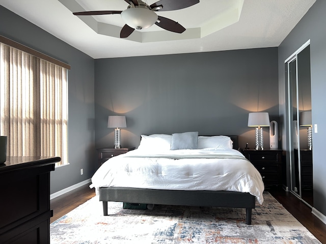 bedroom with ceiling fan, dark hardwood / wood-style floors, and a raised ceiling