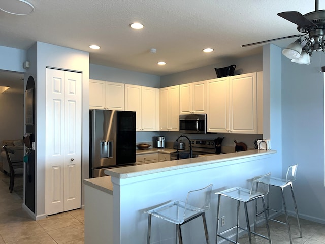 kitchen featuring a breakfast bar area, ceiling fan, white cabinetry, stainless steel appliances, and kitchen peninsula