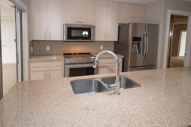 kitchen featuring light stone counters, stainless steel appliances, sink, and decorative backsplash