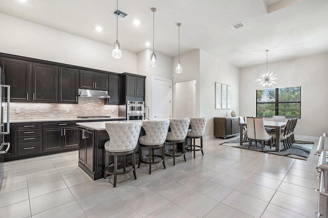 kitchen featuring pendant lighting, a towering ceiling, a breakfast bar, and a kitchen island with sink