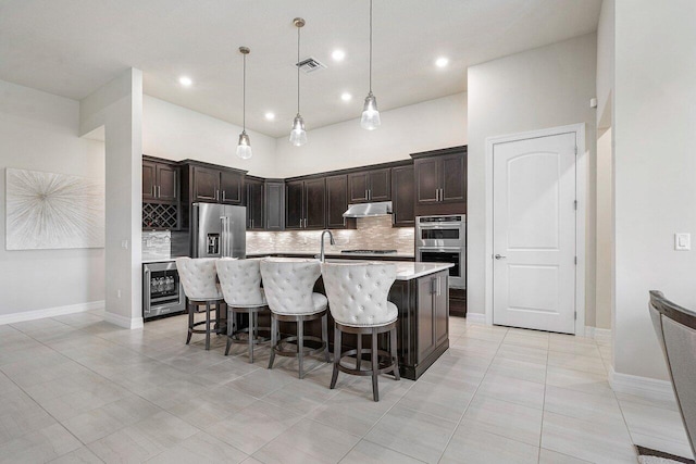 kitchen featuring dark brown cabinetry, a kitchen bar, decorative light fixtures, beverage cooler, and a kitchen island with sink