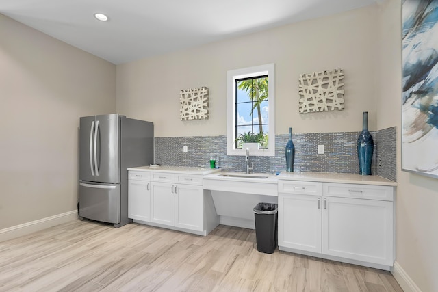 kitchen featuring sink, tasteful backsplash, light wood-type flooring, stainless steel refrigerator, and white cabinets