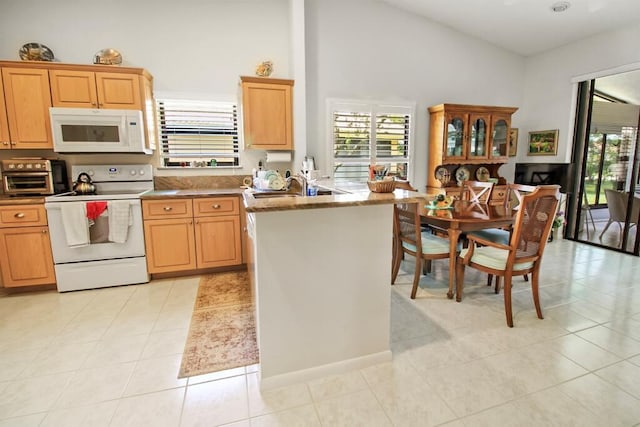 kitchen featuring stone counters, light tile patterned flooring, a towering ceiling, sink, and white appliances