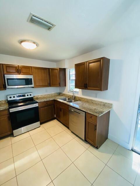 kitchen with appliances with stainless steel finishes, light stone countertops, sink, and light tile patterned floors