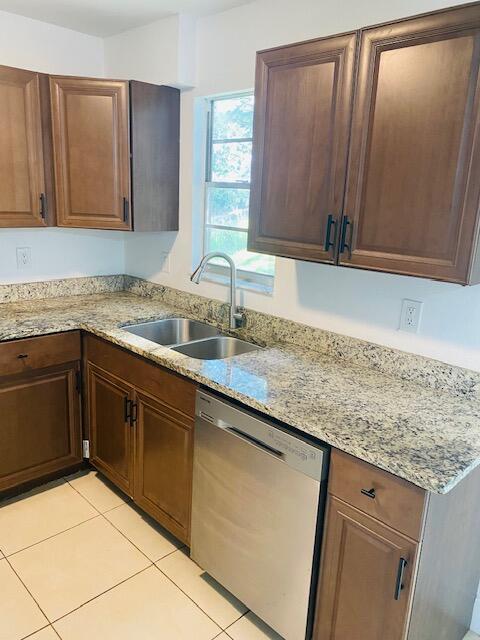 kitchen featuring sink, light stone countertops, dishwasher, and light tile patterned flooring