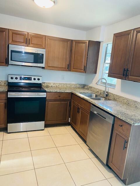 kitchen with light stone counters, stainless steel appliances, sink, and light tile patterned floors