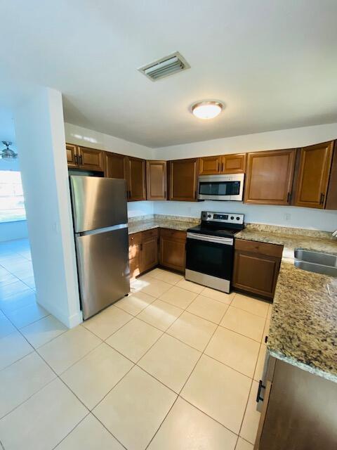 kitchen featuring stainless steel appliances, light tile patterned flooring, sink, and light stone counters