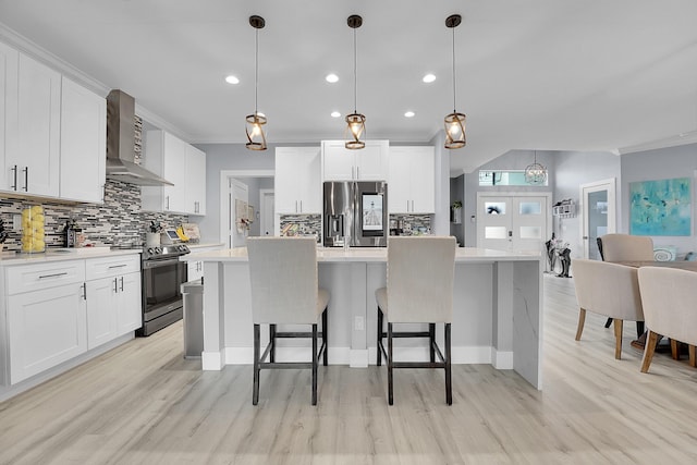 kitchen featuring pendant lighting, wall chimney range hood, stainless steel appliances, white cabinets, and a kitchen island