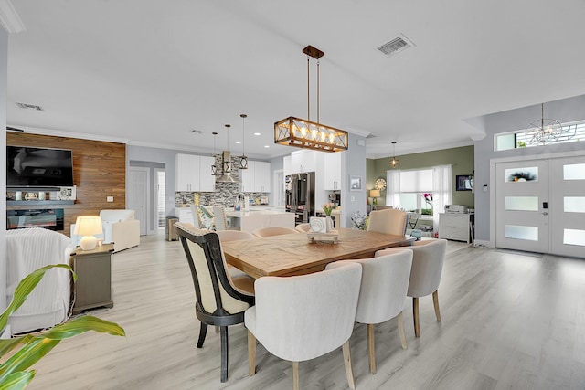 dining area featuring french doors, ornamental molding, light hardwood / wood-style floors, and a notable chandelier