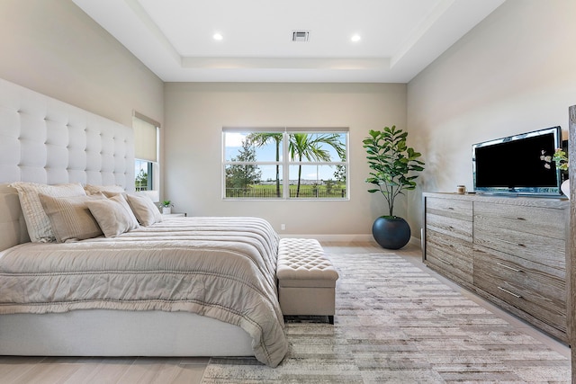 bedroom with a raised ceiling, multiple windows, and light hardwood / wood-style flooring