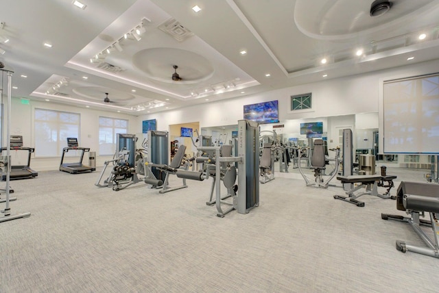 workout area featuring light carpet, a raised ceiling, and ceiling fan