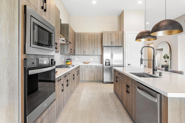 kitchen featuring sink, tasteful backsplash, appliances with stainless steel finishes, pendant lighting, and a kitchen island with sink