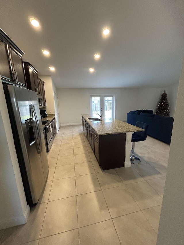 kitchen with an island with sink, sink, a breakfast bar area, light stone counters, and stainless steel appliances