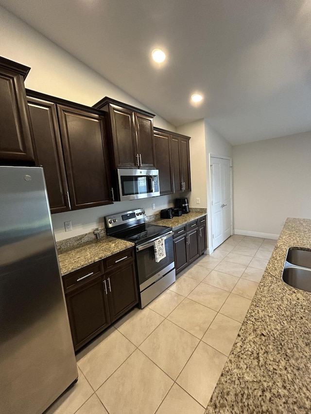 kitchen with stainless steel appliances, vaulted ceiling, dark brown cabinets, and light stone counters