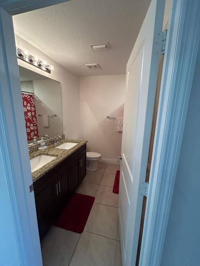 bathroom with tile patterned flooring, vanity, a textured ceiling, and toilet