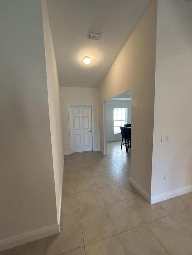 hallway with lofted ceiling, light tile patterned floors, and a textured ceiling