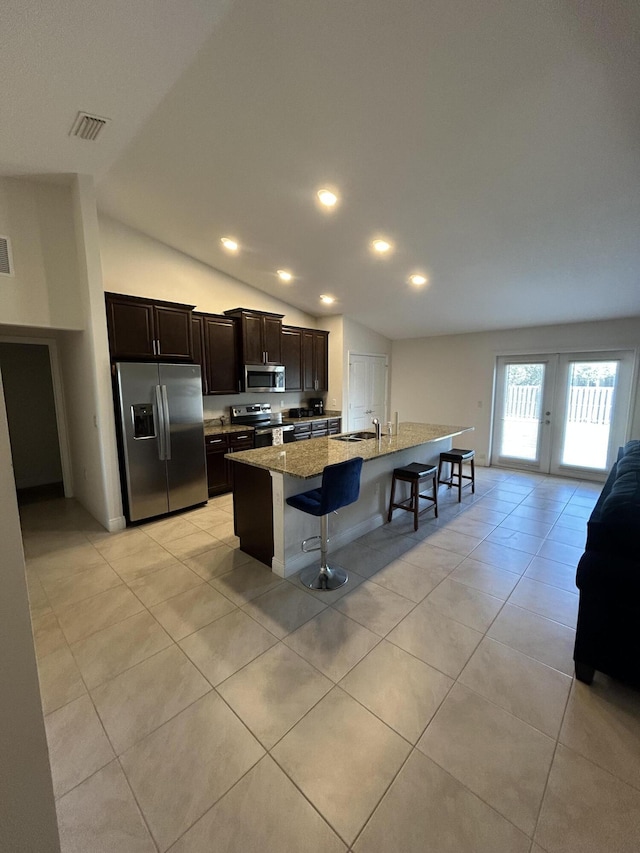 kitchen featuring lofted ceiling, light stone counters, a kitchen breakfast bar, stainless steel appliances, and a kitchen island with sink