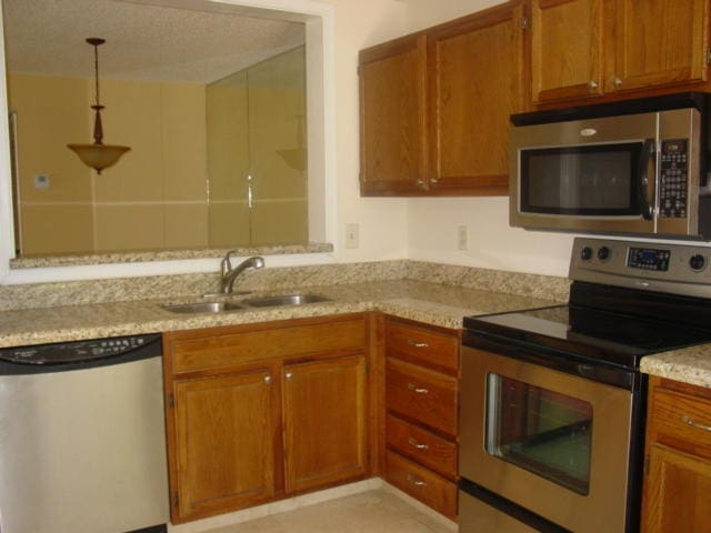 kitchen with sink, light tile patterned floors, appliances with stainless steel finishes, light stone countertops, and decorative light fixtures