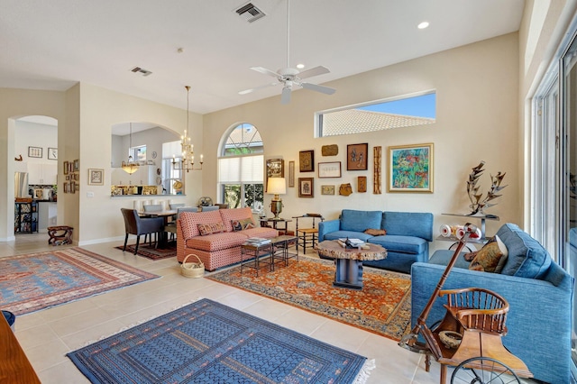 living room with a towering ceiling, ceiling fan with notable chandelier, and tile patterned floors