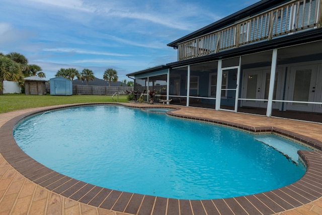 view of pool featuring a patio, an in ground hot tub, a yard, a shed, and a sunroom