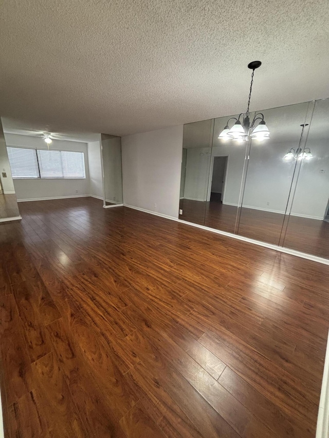 interior space with baseboards, a textured ceiling, dark wood-style flooring, and ceiling fan with notable chandelier