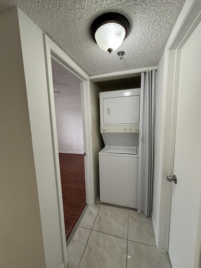 washroom featuring a textured ceiling, stacked washer / dryer, and light tile patterned flooring