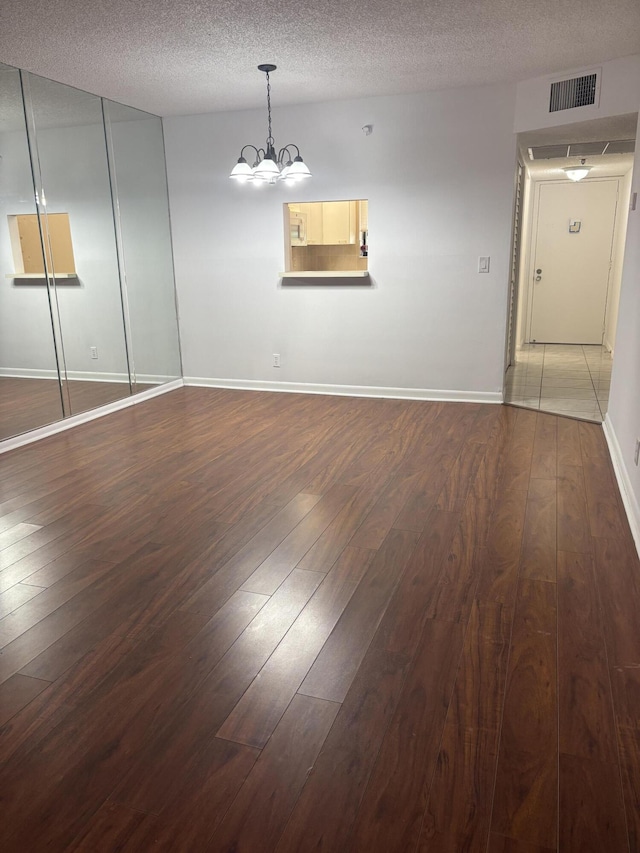 empty room with hardwood / wood-style flooring, baseboards, a chandelier, and a textured ceiling