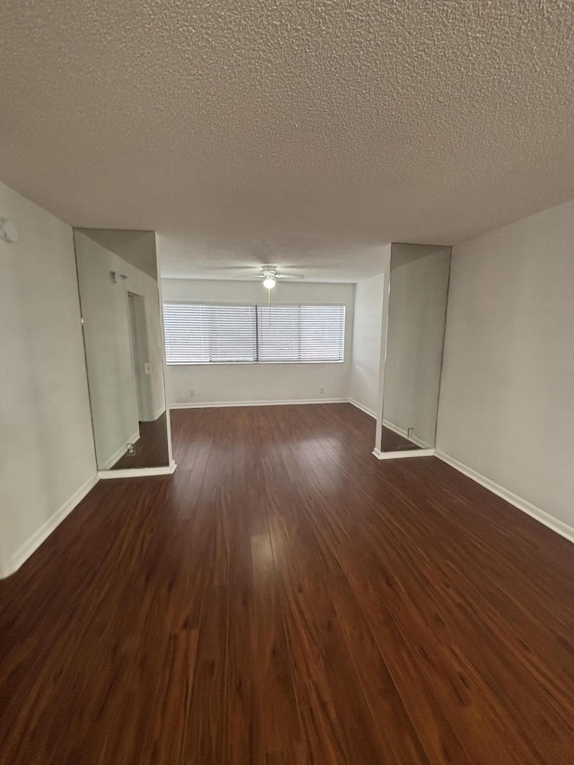 unfurnished living room featuring baseboards, a ceiling fan, dark wood-style flooring, and a textured ceiling